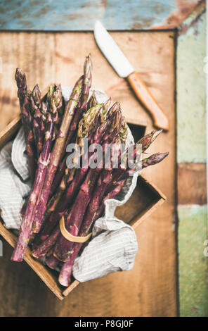 Seasonal harvest produce. Fresh raw uncooked purple asparagus over rustic wooden tray background, selective focus, vertical composition. Local market Stock Photo