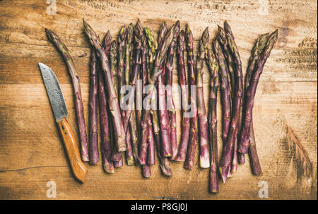 Seasonal harvest produce. Flat-lay of fresh raw uncooked purple asparagus in row over wooden background, top view. Local market food concept Stock Photo