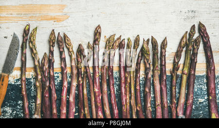 Seasonal harvest produce. Flat-lay of fresh raw uncooked purple asparagus in row over rustic wooden background, top view. Local market food concept Stock Photo