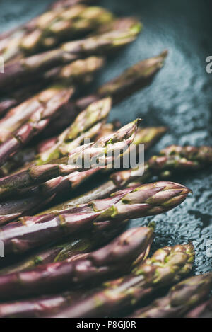 Seasonal harvest produce. Fresh raw uncooked purple asparagus over dark background, selective focus, close-up, vertical composition. Local market food Stock Photo