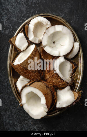 Cracked coconuts arranged in metallic tray on dark textured background. Stock Photo