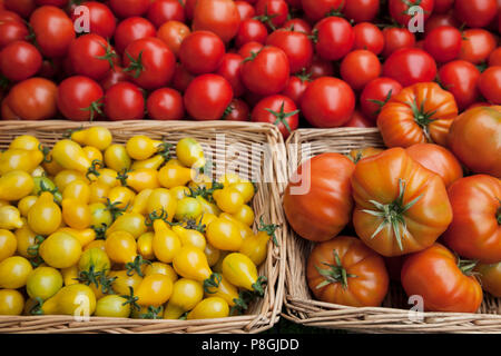 Mixed tomatoes in baskets on market stall Stock Photo