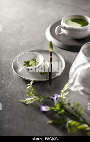 Matcha powder and matcha tea being prepared on a gray concrete countertop in the morning light. Stock Photo