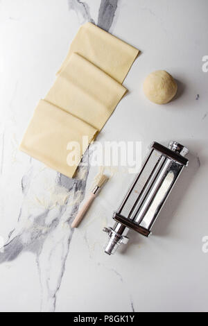 Rolled dough for homemade italian uncooked pasta lasagna from pasta machine maker with semolina flour over white marble texture background. Flat lay, Stock Photo