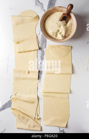 Rolled dough for homemade italian uncooked pasta lasagna from pasta machine maker with semolina flour over white marble texture background. Flat lay, Stock Photo