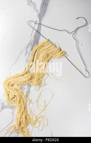 Homemade italian uncooked pasta spaghetti dried on clothes hanger over white marble texture background. Flat lay, space. Stock Photo
