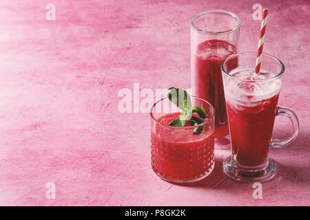 Three different red fruit berry watermelon, strawberry, raspberry, pomegranate cocktails or smoothies in glasses with fresh mint over pink background. Stock Photo