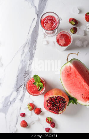 Three different red fruit berry watermelon, strawberry, raspberry, pomegranate cocktails or smoothies in glasses with crushed ice, fresh mint, ingredi Stock Photo