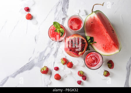 Three different red fruit berry watermelon, strawberry, raspberry, pomegranate cocktails or smoothies in glasses with crushed ice, fresh mint, ingredi Stock Photo