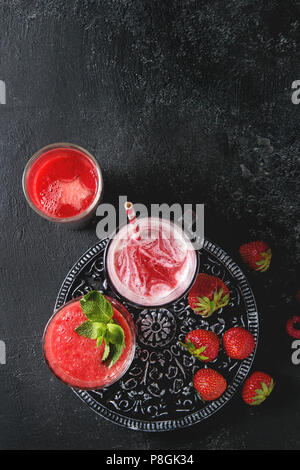 Three different red fruit berry watermelon, strawberry, raspberry, pomegranate cocktails or smoothies in glasses with crushed ice, fresh mint, ingredi Stock Photo