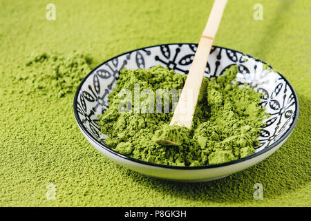 Green tea matcha powder in ceramic bowl with traditional bamboo spoon over powdering matcha as background. Close up Stock Photo