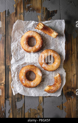 Homemade puff pastry deep fried donuts or cronuts in stack with sugar standing on crumpled paper over dark wooden concrete texture background. Flat la Stock Photo