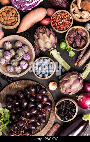 Assortment raw organic of purple ingredients: eggplants, artichokes, potatoes, onions, berries, nuts, carrots, brussel sprouts, grapes over dark backg Stock Photo