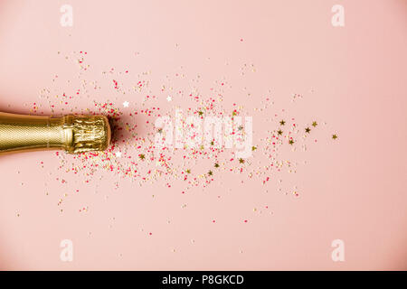 Flat lay of Celebration. Champagne bottle with ice cream sprinkles and golden star sprinkles  on pink background. Top view Stock Photo