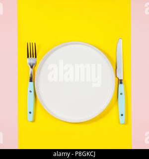 Flat lay of White plate, knife and fork on two color pastel background Stock Photo