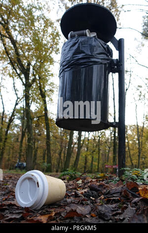 Berlin, Germany, Empty coffee mug lies in front of a full dustbin in the forest Stock Photo