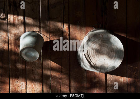 Old tin bucket and washing tub hanging on a weathered wooden plank wall. Stock Photo