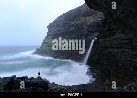 Man looking a a big waterfall falling straight into the ocean at Waterfall Bluff on the Wild Coast of South Africa. Stock Photo