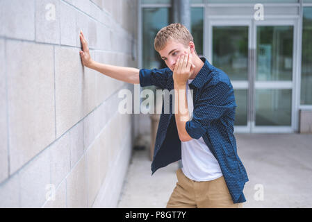 Upset teen leaning against a brick wall outside of a public building. Stock Photo