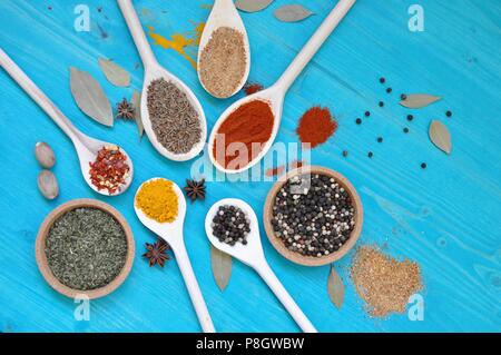 Concept of table with colorful condiments spices in wooden spoons and bowls, on blue background, flat lay, top table