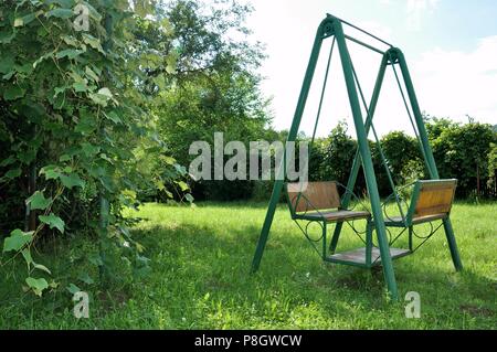 Double rocking chair made of metal and wood in the courtyard of the house in the countryside, green grass background Stock Photo
