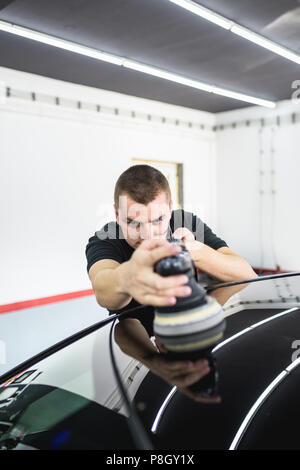 Car detailing - Worker with orbital polisher in auto repair shop. Stock Photo