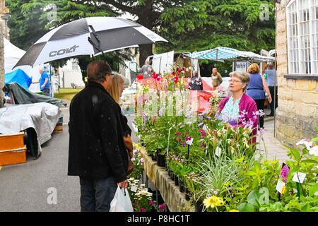 Axminster, Devon, UK.  12th July 2018. UK Weather.  Shoppers in the town of Axminster in Devon with umbrellas up as a light shower passes over on a warm overcast morning.  Picture Credit: Graham Hunt/Alamy Live News Stock Photo