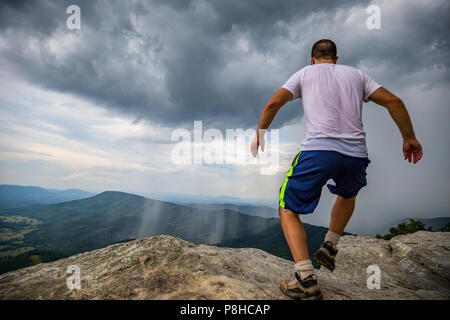 Man Running Towards the edge of  McAfee Knob edge above scenic stormy Valley. Stock Photo