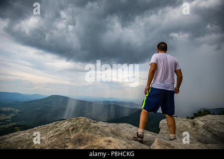 Guy Looking Out into Scenic Stormy Valley Atop McAfee Knob in Virginia with adventure and hope for the future. Rain falling in sheets in the Valley Stock Photo