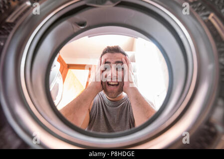 Shocked upset Young man Looking At Stained Bleached Cloth In Washing Machine. View from the inside of washing machine. Stock Photo