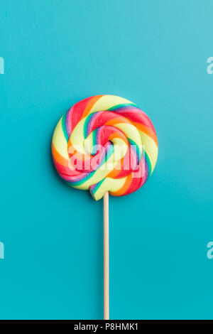Colorful rainbow swirl lollipop on blue background. Stock Photo