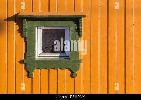 Square window in bright yellow painted timber wall with green frame. Closeup fragment of house exterior Stock Photo