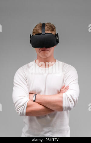Man wearing virtual reality goggles on gray background. Student using VR headset. Stock Photo