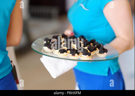 Waitress holding a dish of blackberry cupcakes Stock Photo