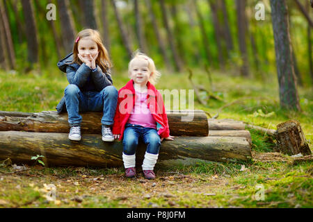 Two little sisters sitting on a big log in a forest Stock Photo