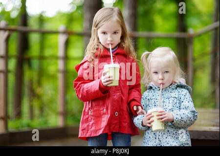 Two little sisters drinking hot cholocate in summer park on beautiful autumn day Stock Photo