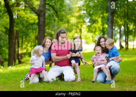 Happy big family of three adults and four kids having fun in summer park Stock Photo