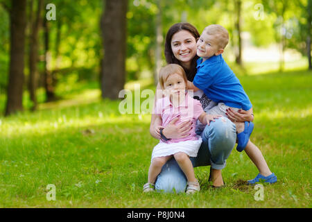 Young mother and her two adorable little kids having fun in summer park on beautiful sunny day Stock Photo
