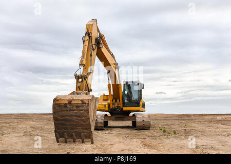 heavy yellow excavator with backhoe parked on construction site against dramatic sky Stock Photo