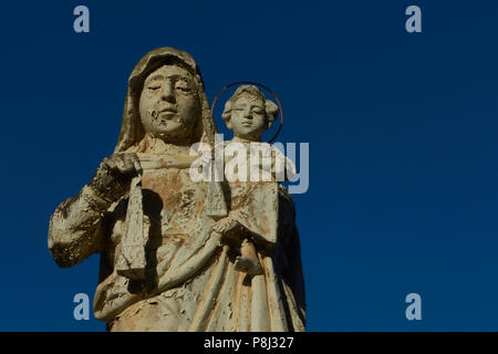 A weather worn statue looking down in the Addolorata Cemetery, Paola, Malta, with a clear blue sky behind Stock Photo