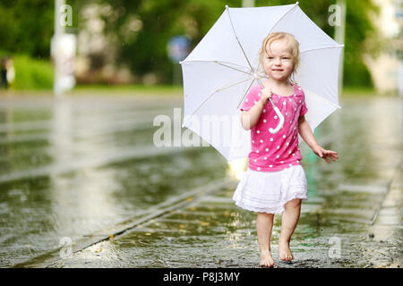 Cute little toddler girl standing in a puddle holding umbrella on a rainy summer day Stock Photo