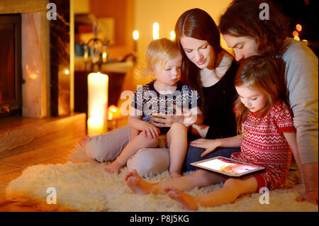 Happy young family using a tablet pc at home by a fireplace in warm and cozy living room on winter day Stock Photo