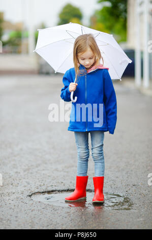 Adorable little girl holding white umbrella standing in a puddle on warm autumn day Stock Photo