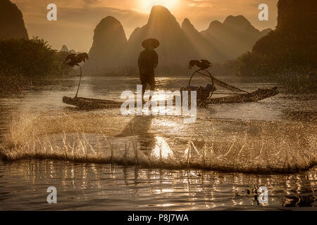 Cormorant Fisherman casting net on Li river, Xingping, Guilin China, as the sun sets behind the karst mountains behind him. Stock Photo