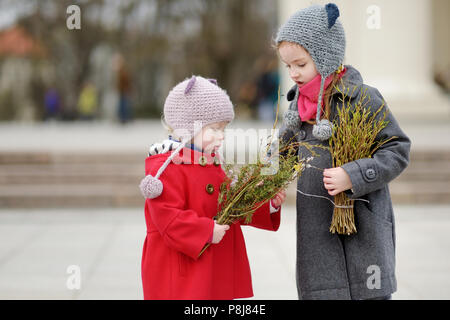 Two adorable little sisters holding willow branches and other plants as part of Easter tradition in Lithuania Stock Photo