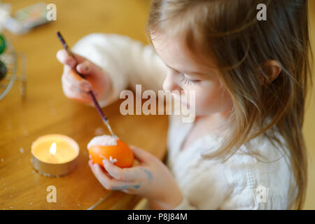 Adorable little girl coloring an Easter egg using wax and dyes Stock Photo