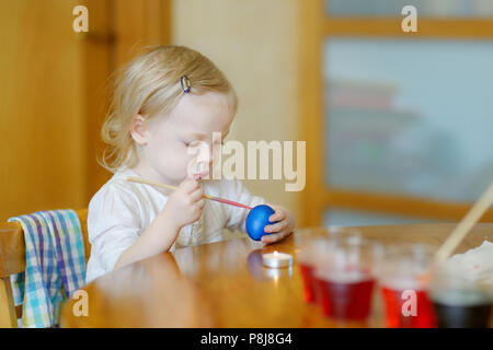 Adorable little girl coloring an Easter egg using wax and dyes Stock Photo