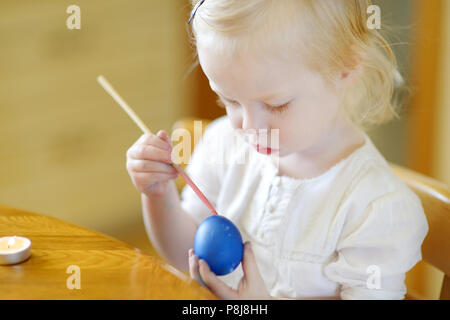 Adorable little girl coloring an Easter egg using wax and dyes Stock Photo