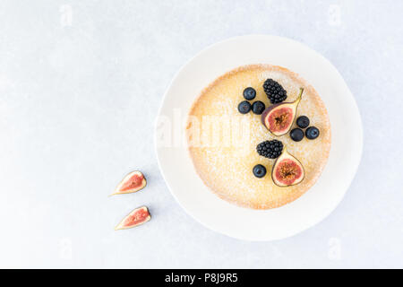 Top view of a lemon tart decorated with figs, blueberries and blackberries on light blue background with copy space. Stock Photo
