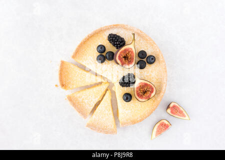 Lemon tart sliced and decorated with fresh figs, blueberries and blackberries on light gray background with copy space. Top view. Stock Photo